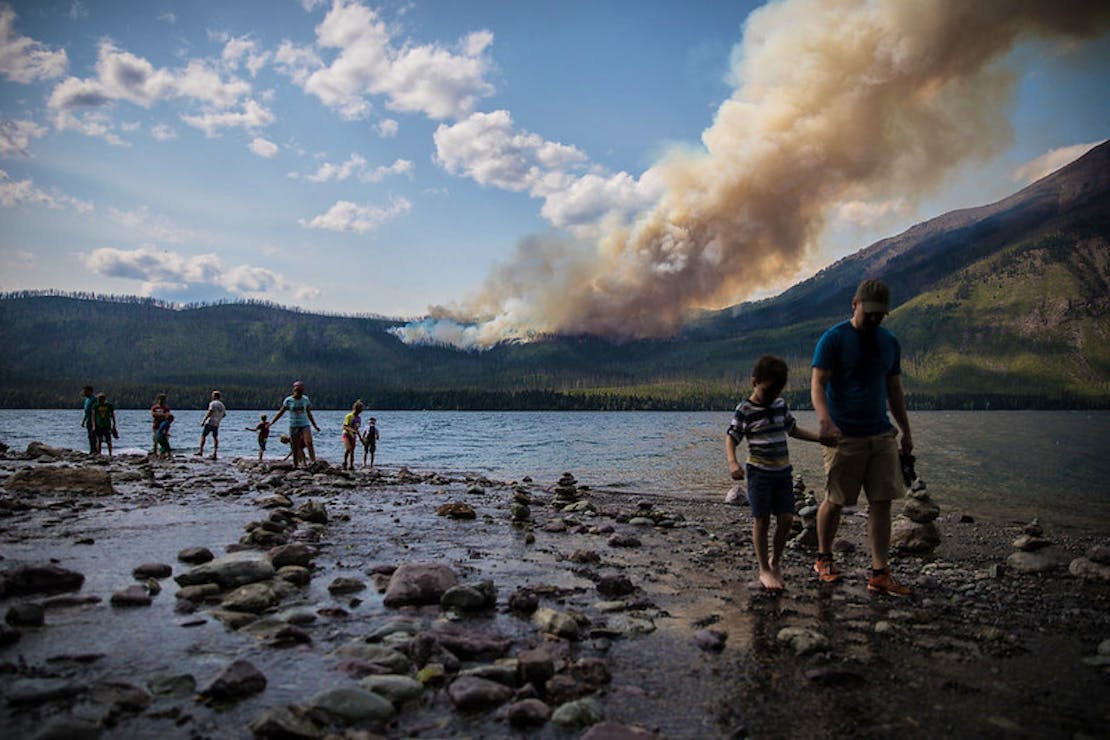 The Howe Ridge Fire from Lake McDonald Lodge with people walking around the lake edge