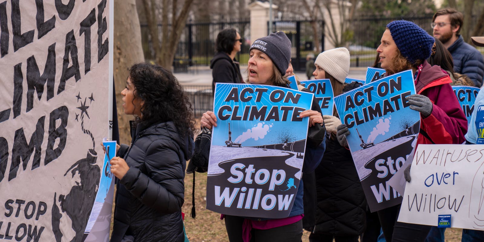 People with hats on at an outdoor rally holding signs that read messages asking to Stop Willow.