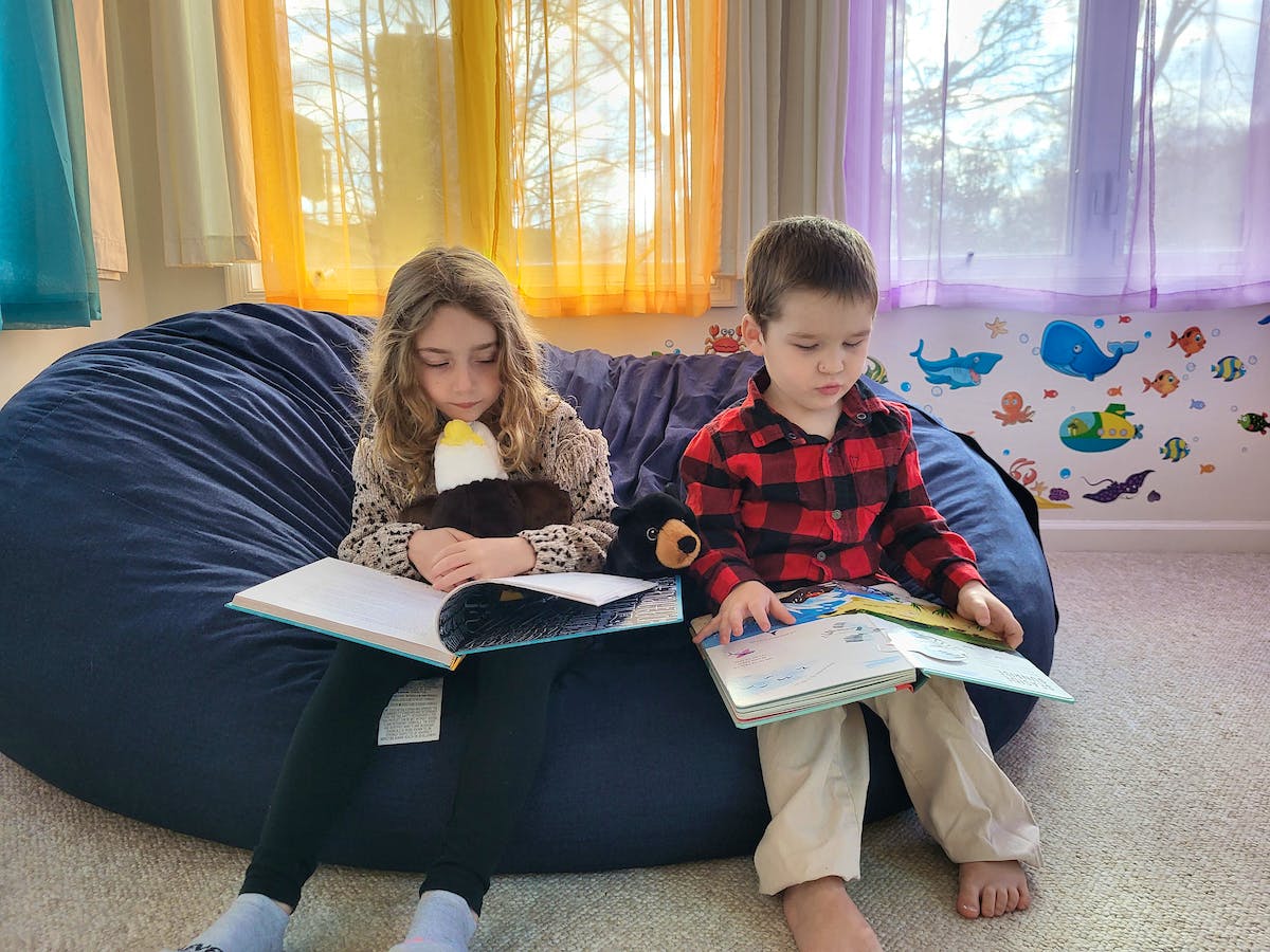 two kids sitting on a beanbag with plushies and books