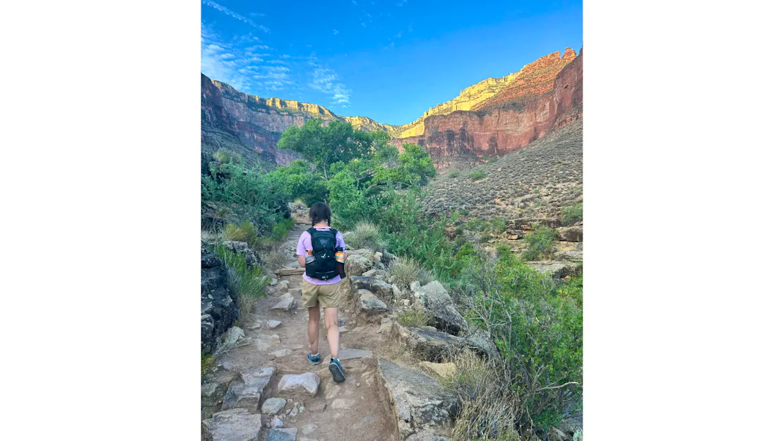 Megan, a young female, hikes along a rocky trail in the Grand Canyon. She is wearing a navy blue backpack.