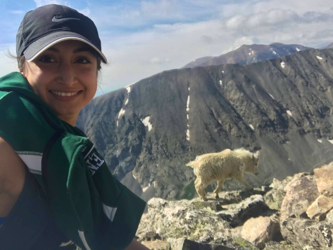A selfie of Field Representative, Azalia, on a hike with a furry, white mountain goat in the background. 