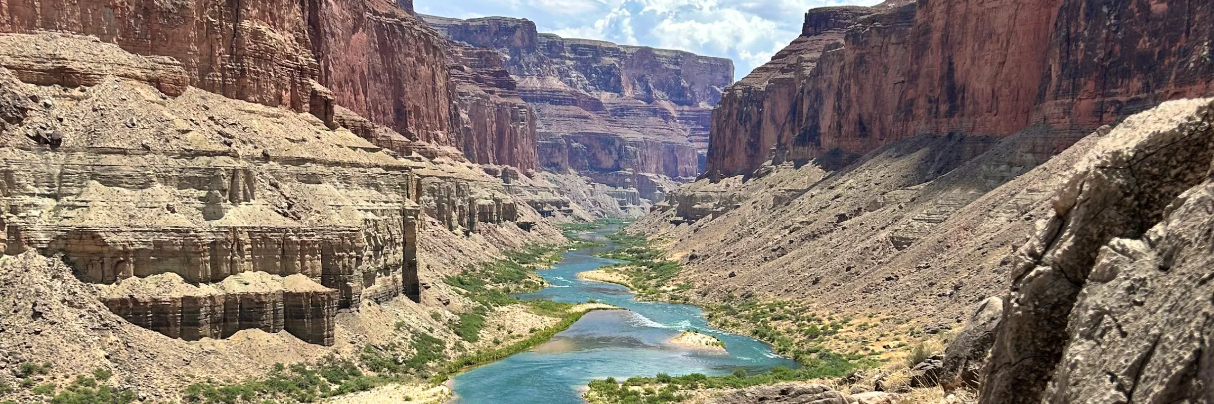 A landscape photo of Grand Canyon National Park. A river cuts through the center of the photo, splitting the canyon's red walls rising on either side.