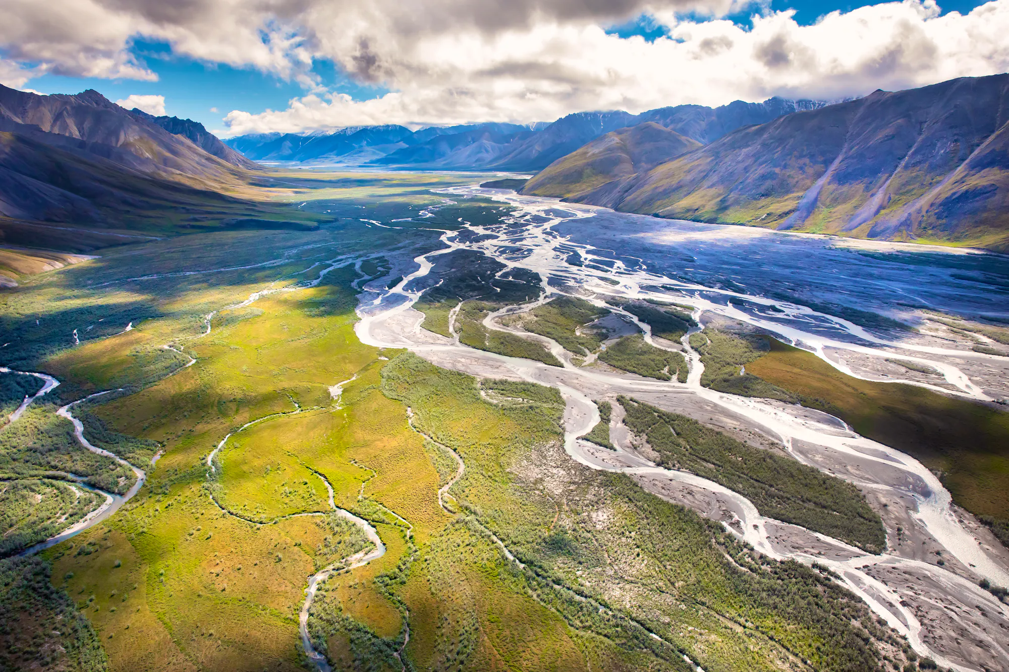 Arctic National Wildlife Refuge in Alaska. A green landscape with brown mountains rising in the distance on either side and in the far background. 