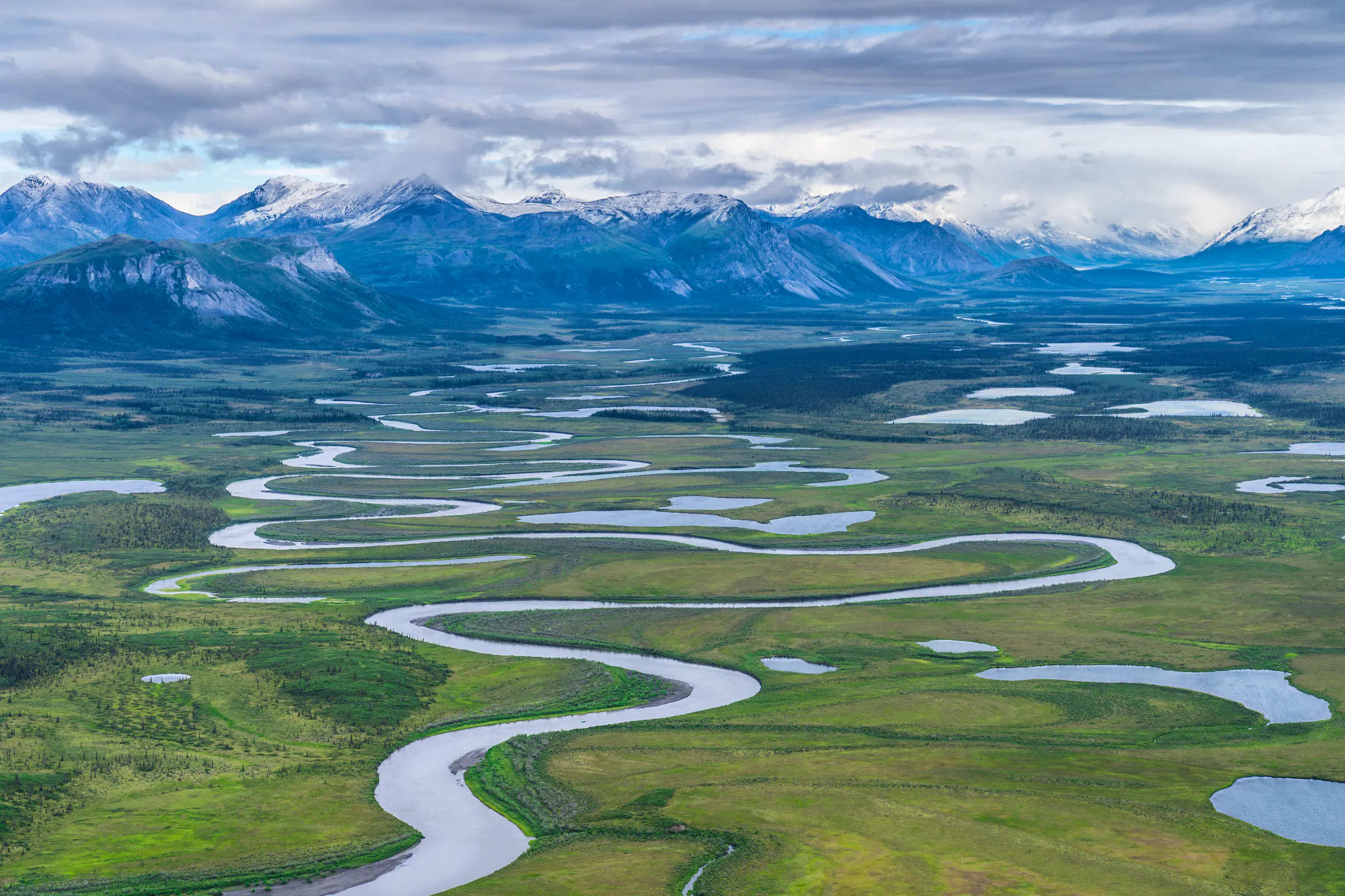 The Sheenjek River winds its way across the plain at Arctic National Wildlife Refuge in Alaska with mountains in background
